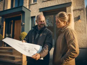 Entrepreneur/expert expliquant le plan fini au propriétaire devant la façade rénovée